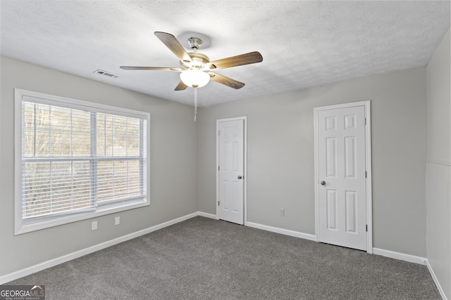 unfurnished bedroom with a textured ceiling, dark carpet, visible vents, and baseboards