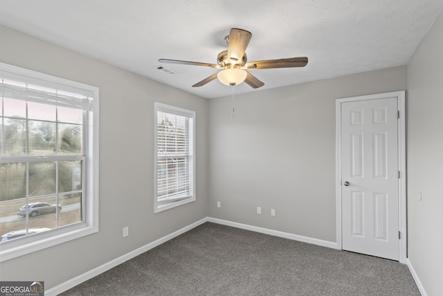 spare room with baseboards, visible vents, dark carpet, and ceiling fan