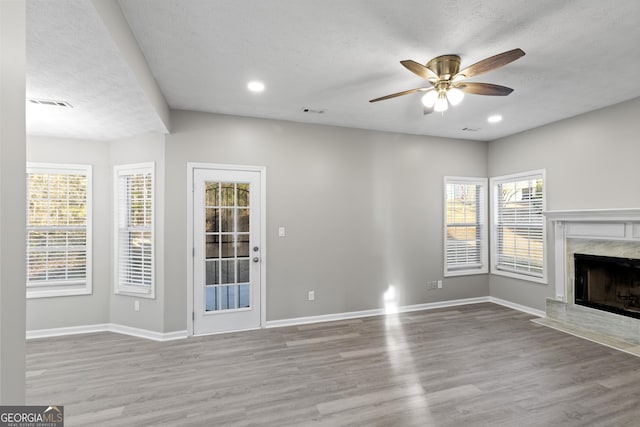 unfurnished living room featuring ceiling fan, baseboards, wood finished floors, and a high end fireplace
