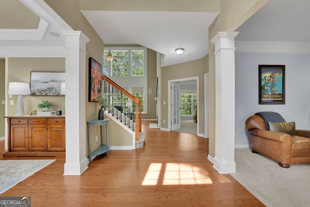 foyer entrance featuring light wood-style flooring, stairway, and ornate columns