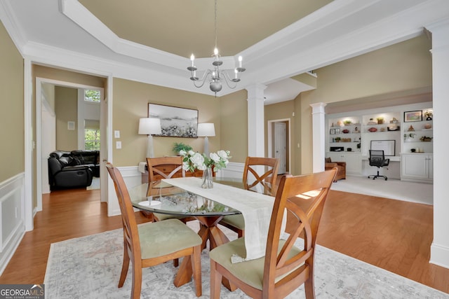 dining space with a raised ceiling, a chandelier, ornate columns, wood finished floors, and ornamental molding