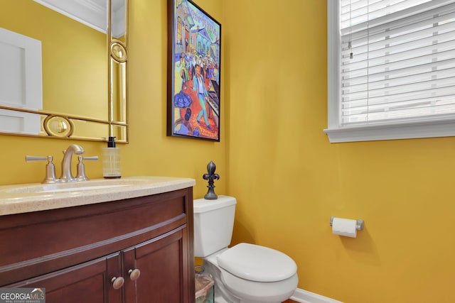 half bath featuring baseboards, vanity, and toilet