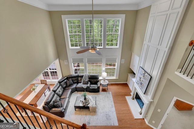 living room featuring baseboards, a high ceiling, a ceiling fan, and light wood-style flooring