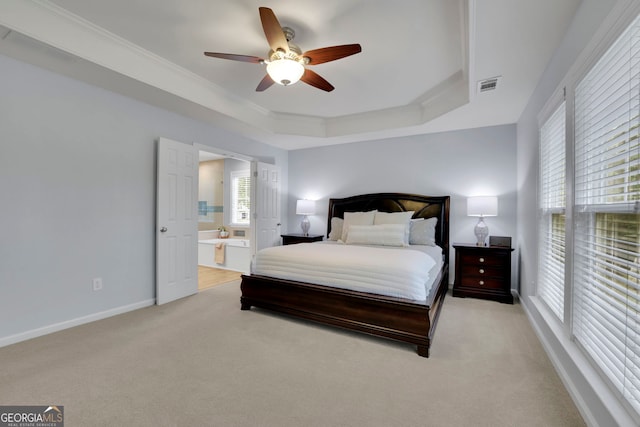 bedroom with a tray ceiling, visible vents, ornamental molding, light carpet, and ensuite bathroom