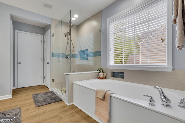 bathroom with a bath, a shower stall, wood finished floors, and visible vents