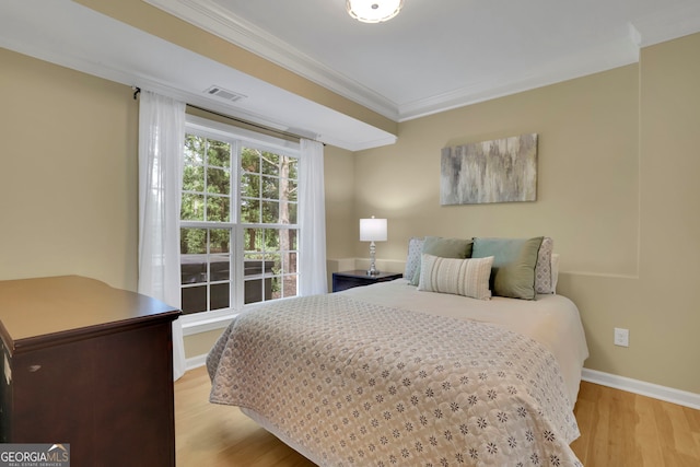 bedroom with wood finished floors, visible vents, baseboards, and ornamental molding