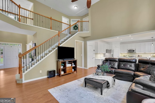 living room featuring light wood finished floors, a towering ceiling, stairs, and a ceiling fan