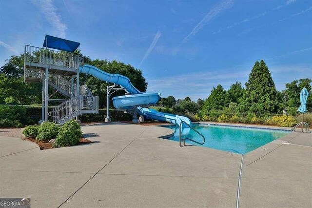 pool with a patio area, a water slide, and stairs