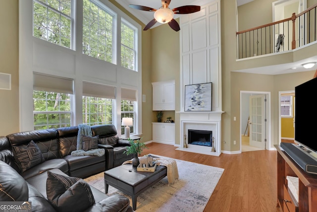 living area with light wood-style floors, a high ceiling, a ceiling fan, and a wealth of natural light