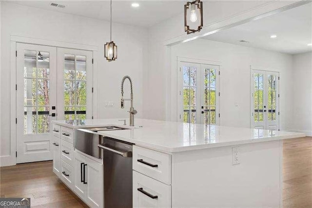 kitchen featuring wood finished floors, stainless steel dishwasher, french doors, pendant lighting, and white cabinetry