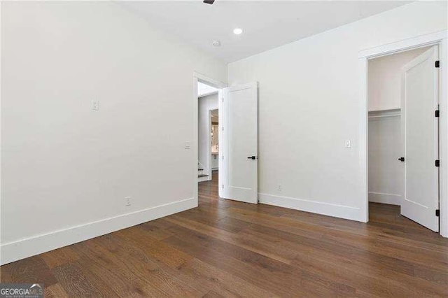 unfurnished bedroom featuring wood finished floors, baseboards, a closet, and a walk in closet