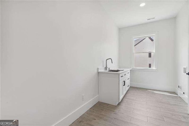 laundry area with cabinet space, light wood finished floors, baseboards, and a sink