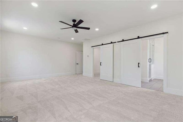 unfurnished bedroom with a barn door, baseboards, recessed lighting, light colored carpet, and a ceiling fan