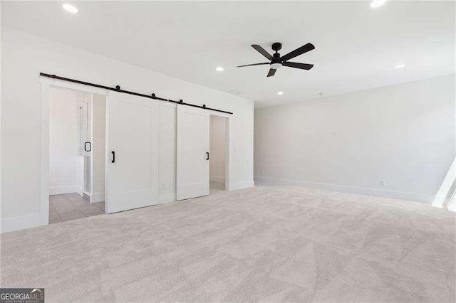 unfurnished bedroom featuring a barn door, recessed lighting, a ceiling fan, light carpet, and baseboards