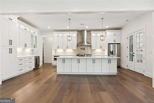 kitchen featuring dark wood finished floors, wall chimney exhaust hood, stainless steel appliances, and light countertops