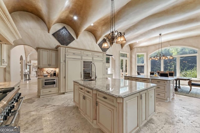 720 Heards Ferry Rd, Atlanta, GA 30328 - kitchen featuring an island with sink, cream cabinetry, a sink, arched walkways, and appliances with stainless steel finishes