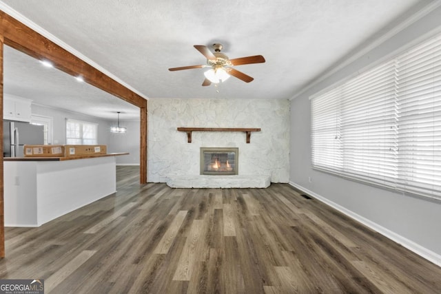 unfurnished living room with a stone fireplace, baseboards, ceiling fan with notable chandelier, and dark wood-style floors