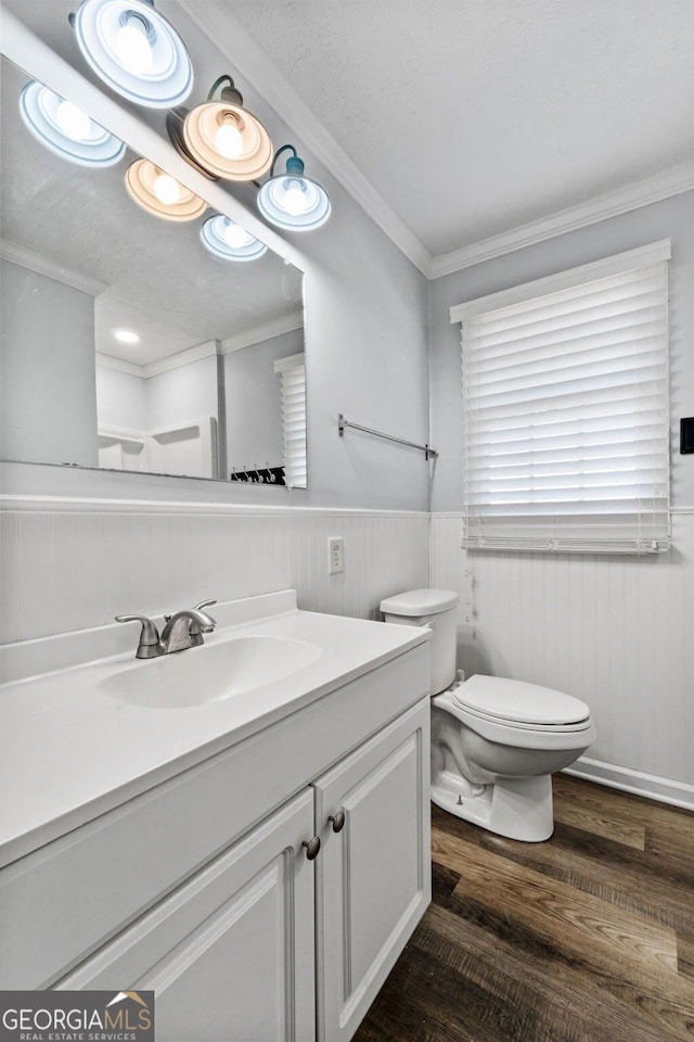 bathroom featuring wood finished floors, a wainscoted wall, vanity, toilet, and ornamental molding