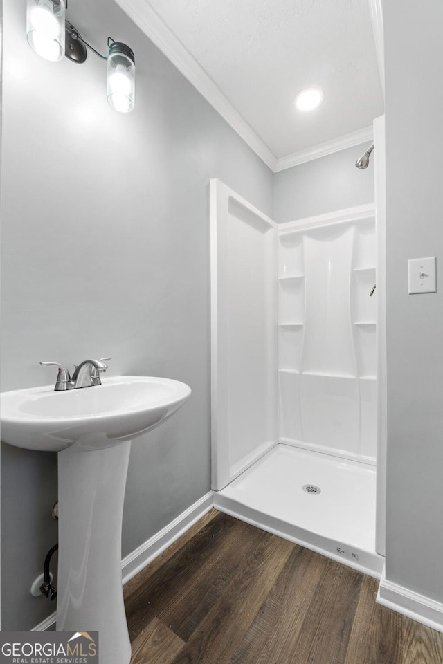 bathroom with crown molding, wood finished floors, baseboards, a shower stall, and a sink