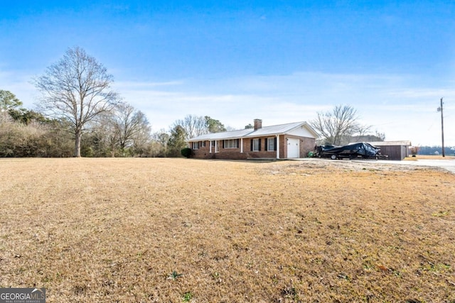 ranch-style house with a chimney, a front yard, a garage, brick siding, and concrete driveway