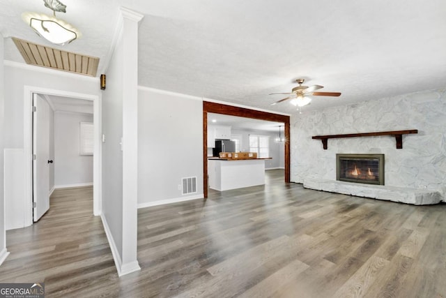 unfurnished living room featuring visible vents, a ceiling fan, wood finished floors, and a stone fireplace
