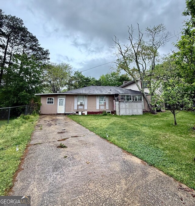 ranch-style home featuring concrete driveway, brick siding, fence, and a front yard