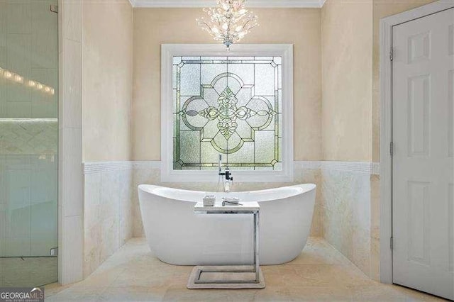 bathroom with a wainscoted wall, tile walls, a freestanding bath, and a chandelier