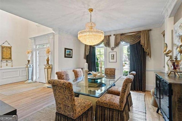 dining area featuring light wood-style floors, crown molding, a notable chandelier, and wainscoting