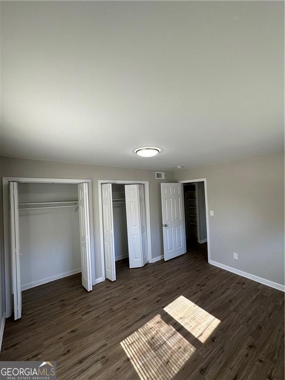 1401 Vesta Ave, East Point, GA 30344 - unfurnished bedroom featuring two closets, baseboards, dark wood-type flooring, and visible vents