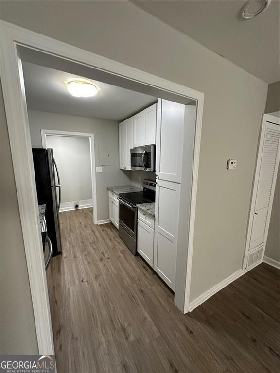 1401 Vesta Ave, East Point, GA 30344 - kitchen with dark wood finished floors, baseboards, appliances with stainless steel finishes, and white cabinets