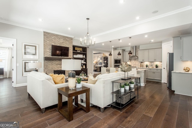 living area featuring a brick fireplace, a chandelier, dark wood-type flooring, and ornamental molding