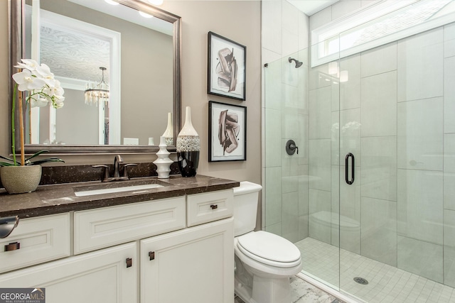 bathroom featuring a notable chandelier, vanity, a shower stall, and toilet