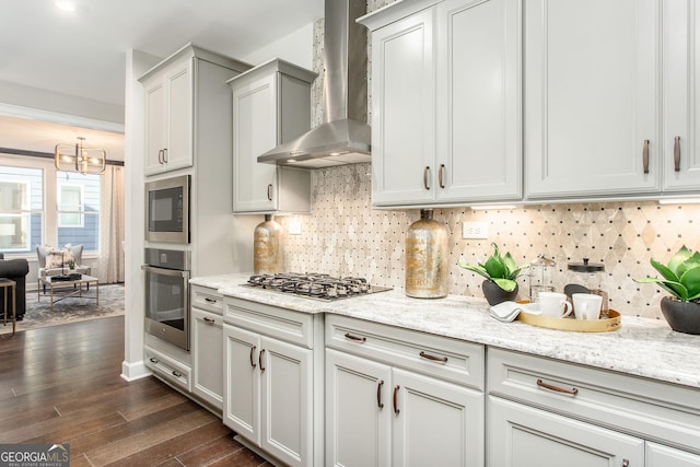 kitchen with wall chimney range hood, stainless steel gas cooktop, an inviting chandelier, backsplash, and dark wood-style floors
