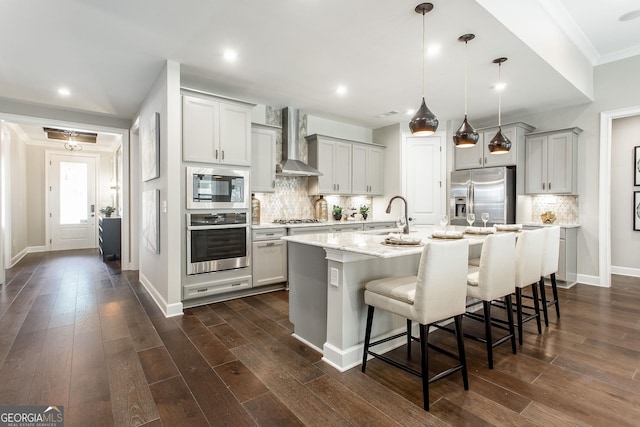 kitchen with dark wood-type flooring, wall chimney exhaust hood, appliances with stainless steel finishes, and a kitchen breakfast bar