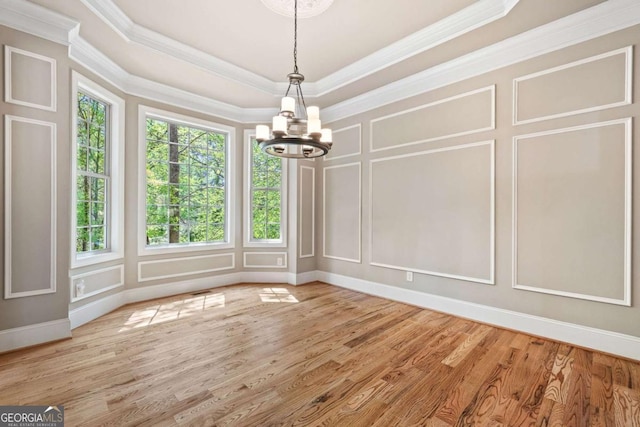 unfurnished dining area with a decorative wall, ornamental molding, wood finished floors, and an inviting chandelier