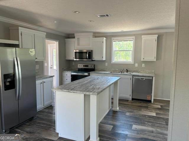 908 Bethel Freewill Rd, Baxley, GA 31513 - kitchen featuring appliances with stainless steel finishes, ornamental molding, white cabinets, dark wood-type flooring, and a center island