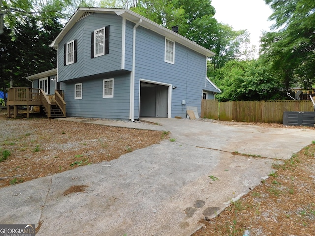 exterior space featuring concrete driveway, a wooden deck, an attached garage, fence, and stairway