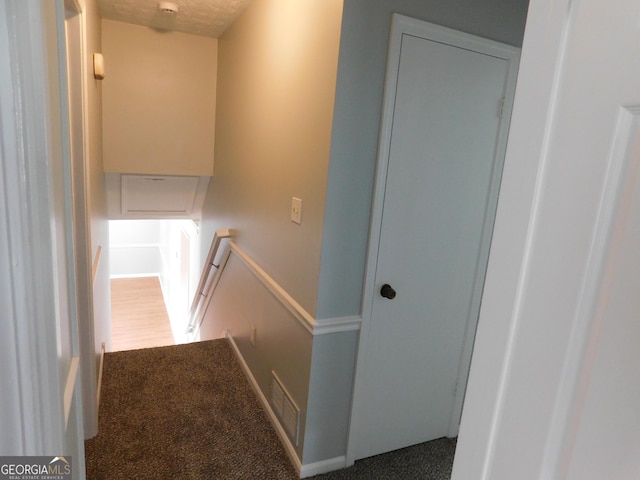 hall with visible vents, an upstairs landing, and carpet floors