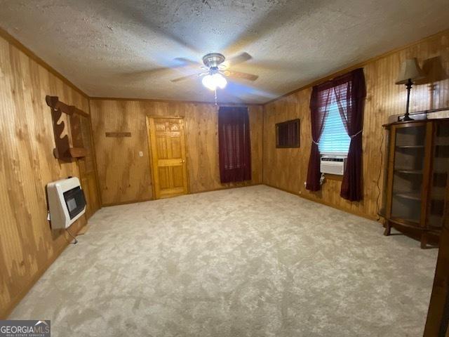 unfurnished living room featuring heating unit, carpet flooring, wood walls, and ceiling fan