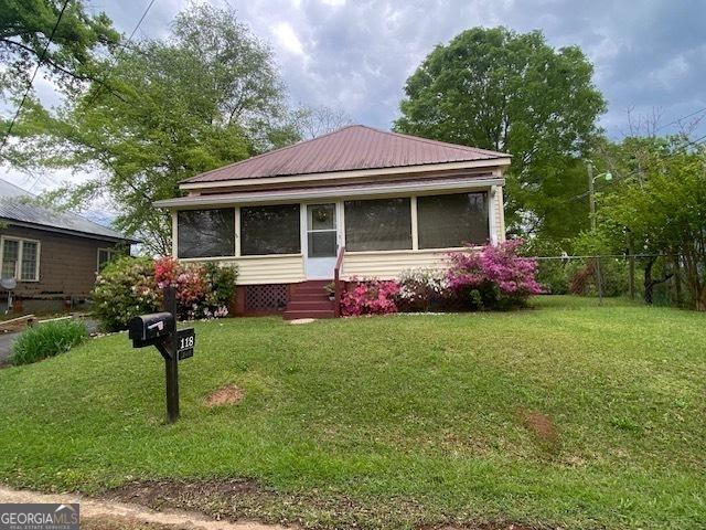 bungalow-style house featuring a front yard, a sunroom, metal roof, and fence