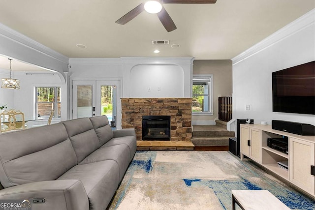 living area with wood finished floors, visible vents, a stone fireplace, ornamental molding, and ceiling fan