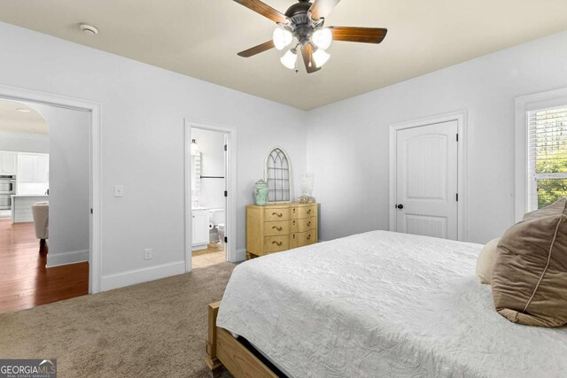 bedroom featuring carpet, a ceiling fan, arched walkways, ensuite bath, and baseboards
