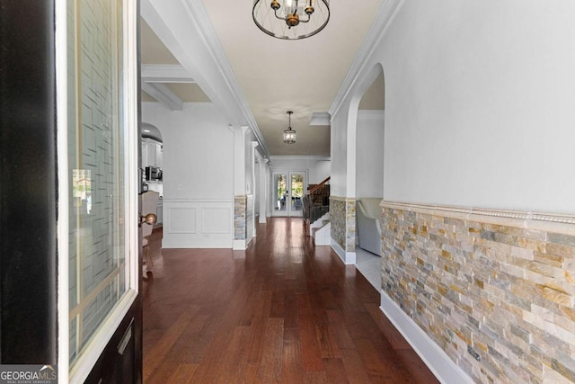 hall with dark wood finished floors, a wainscoted wall, arched walkways, crown molding, and a chandelier