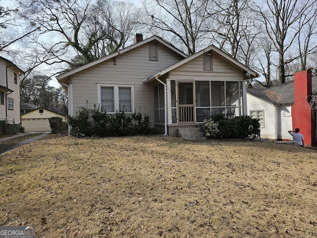 bungalow-style home with a sunroom, a front yard, and a chimney