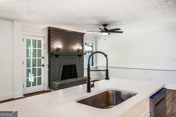 kitchen with a sink, a textured ceiling, a ceiling fan, a brick fireplace, and dishwasher