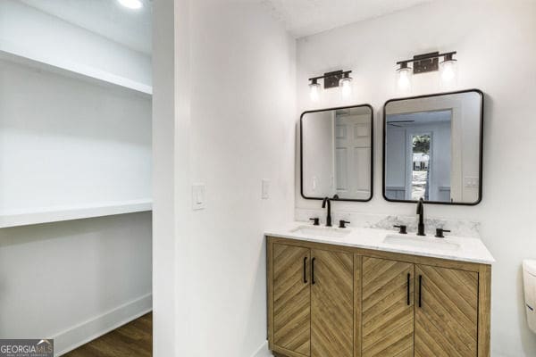 full bathroom with baseboards, a sink, double vanity, and toilet