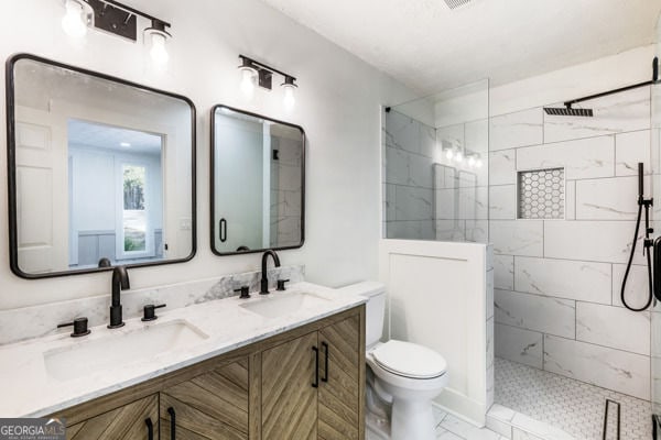 bathroom featuring double vanity, walk in shower, toilet, and a sink