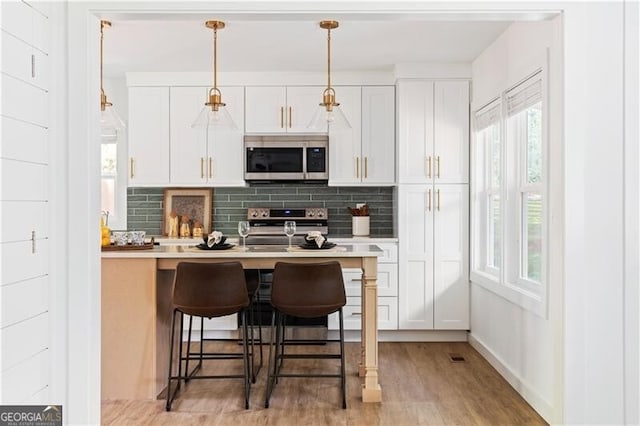 2086 Harold Ave SE, Smyrna, GA 30080 - kitchen featuring stainless steel appliances, decorative backsplash, light wood-type flooring, a kitchen breakfast bar, and light countertops