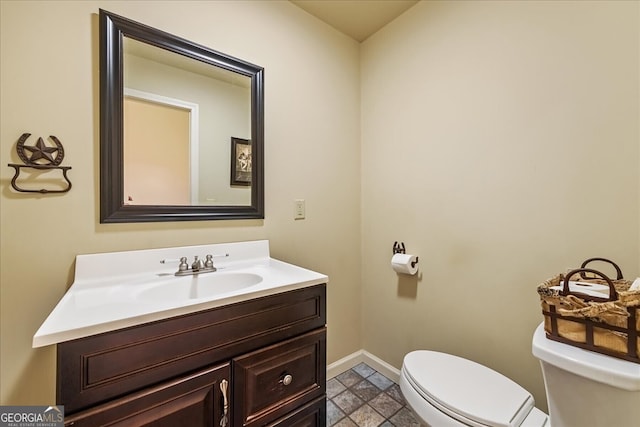 half bathroom with stone finish floor, vanity, toilet, and baseboards