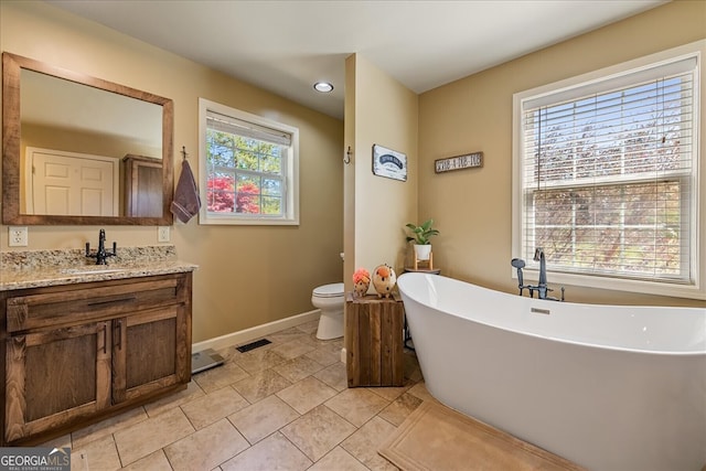 bathroom with vanity, baseboards, a freestanding bath, toilet, and visible vents